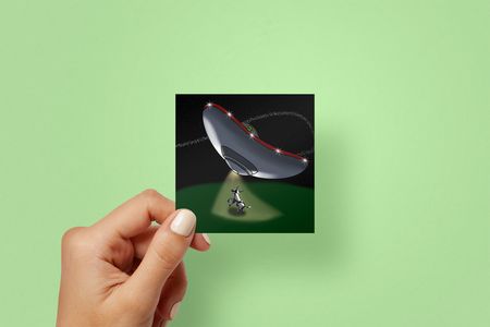 image of the sticker being held by a person - the image includes an alien space ship swooping through the sky to pick up their cow friend to go off on alien adventures