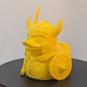 A yellow 3D printed rubber duck inspired piece, dressed like a fantasy fighter with a shield, large sword, and a horned helmet.