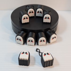 A group of ten ghost clickers. Half of them have ball chains coming out of the top of their holders. Each one has a white stereotypical ghost as one part, printed in white with black eyes and red cheeks. They are in a black base that surrounds them.